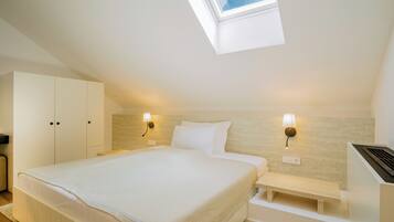 A bedroom with a skylight, a bed with white bedding, two bedside lamps, a wooden bench, and a wardrobe.