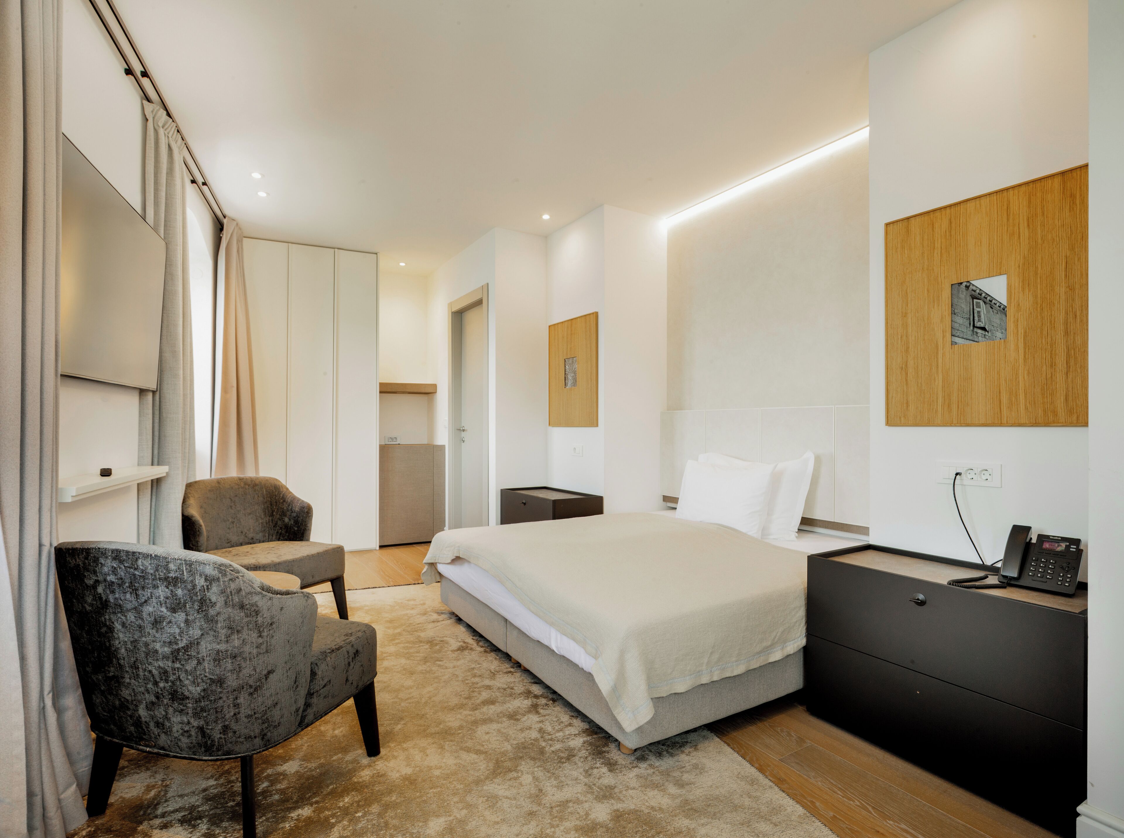 A modern hotel room with a bed, a desk, a chair, and a TV.