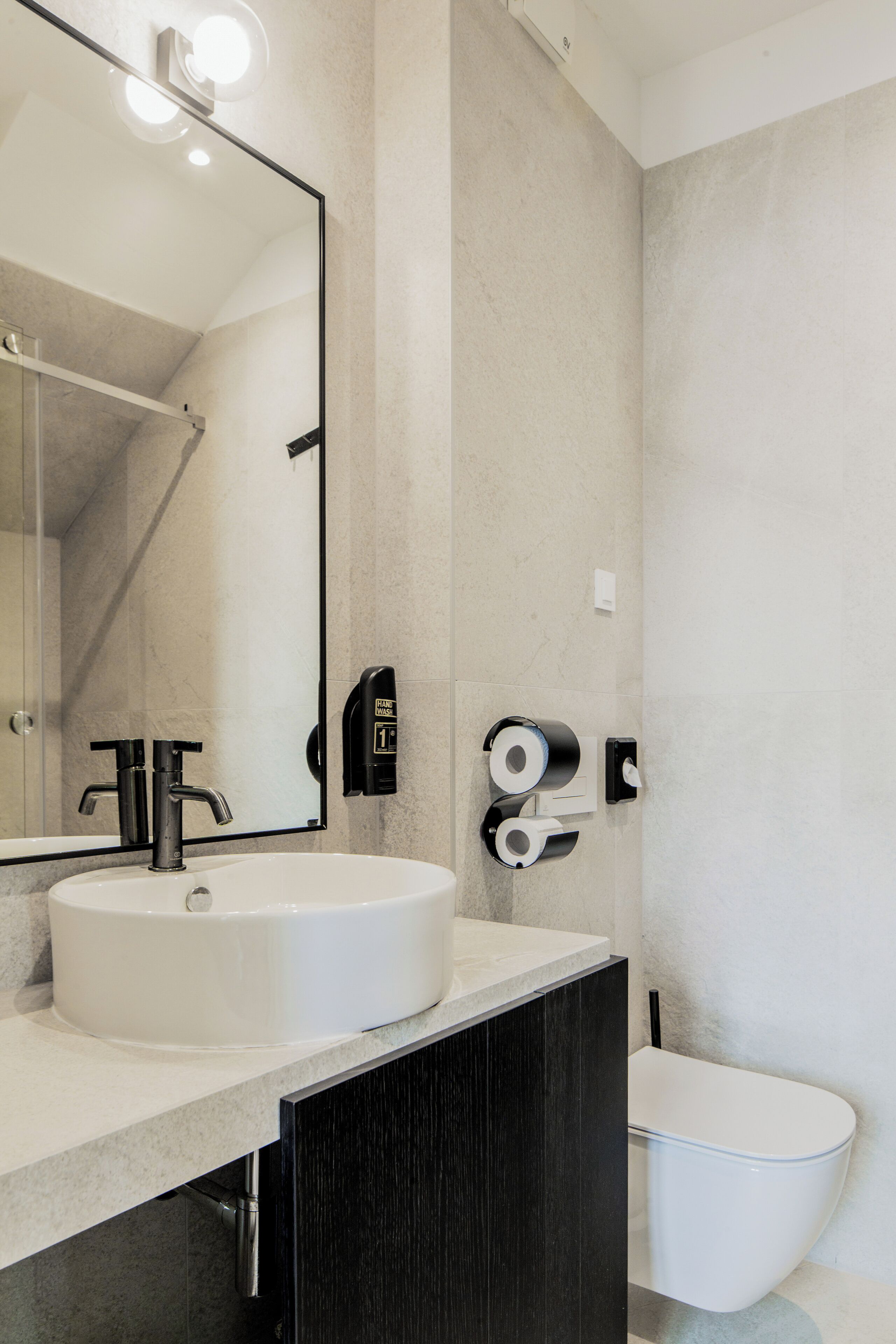 Een moderne badkamer met een grote spiegel, een witte wastafel, een toilet en een douchehoek.