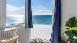 Habitación con vista a la playa y al océano a través de una ventana con cortinas azules.