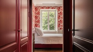 A narrow hallway leading to a bedroom with a window, wooden flooring, and red wallpaper. - Deluxe double room (Le Pian-Médoc)