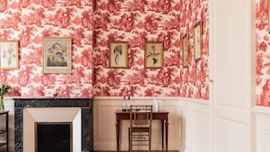A room with a fireplace, a wooden table with chairs, and a patterned wallpaper. - Deluxe double room (Le Pian-Médoc)