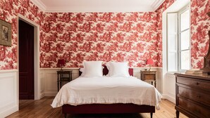 A bedroom with a large bed, floral wallpaper, wooden flooring, and a dresser. - Deluxe double room (Le Pian-Médoc)