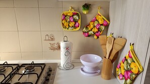 A kitchen with a gas stove, a white paper towel holder, a white bowl, wooden utensils, and fruit-patterned oven mitts. - Cool apartment with AC in Piombino (Piombino)