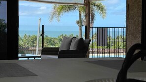 A balcony with a view of the ocean, a wicker chair, and a table with a white tablecloth. - Le Reve Wake up to sunrises and tropical breezes (Mission Beach)