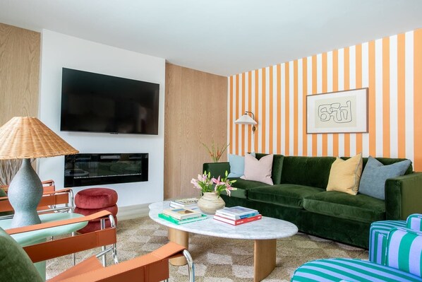 A modern living room with a green sofa, striped wallpaper, a flat-screen TV, and a lamp. - Fun Stylish Scottsdale Retreat | Pool, Paint & Sip (Scottsdale)