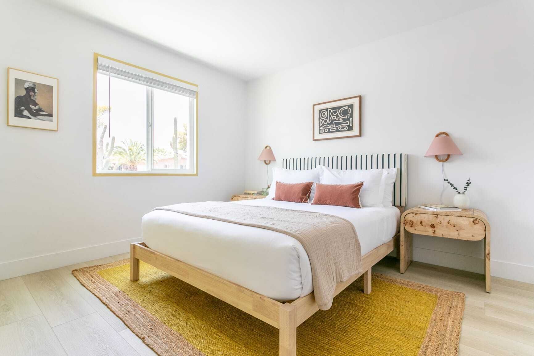 A bedroom with a bed, bedside tables, a window, and artwork on the walls.