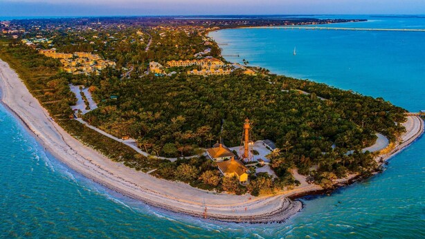 An aerial view of a coastal area with a lighthouse, clear blue waters, and a sandy beach. - 11751 Pasetto Ln #306 (Fort Myers)