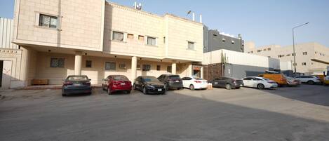 Un estacionamiento con varios coches aparcados frente a un edificio de fachada color crema y múltiples ventanas.