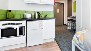 A compact kitchen with white cabinets, a microwave, and a kettle. There is a small dining area with a table and chairs. - Studios and Ensuites at St James Point in Newcastle (Newcastle-upon-Tyne)