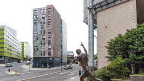 A statue of a figure in motion, a modern building with a green facade, and a street with cars and a pedestrian crossing. - Studios and Ensuites at St James Point in Newcastle (Newcastle-upon-Tyne)