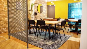 A dining area with a wooden table, black chairs, a patterned rug, a brick wall, and a yellow wall with a window. - Studios and Ensuites at St James Point in Newcastle (Newcastle-upon-Tyne)
