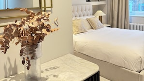 Une chambre moderne avec un grand lit, une table de chevet ornée d’un vase contenant des feuilles séchées et un grand miroir avec un cadre doré.