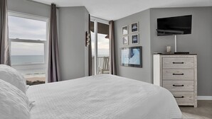 A bedroom with a large bed, a TV, and a dresser. - Stunning 2 bedroom, oceanfront condo (North Topsail Beach)