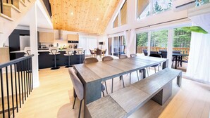 A modern kitchen with a wooden ceiling, a dining area with a long table and chairs, and a view of a deck. - Spa - Pool table | Great Comfort | Chalet Le Mysa (Shannon)
