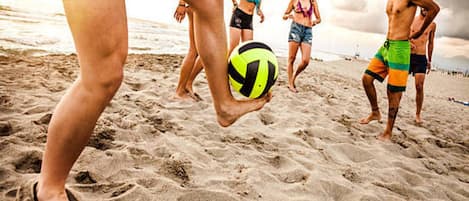 A beach scene with people playing volleyball.