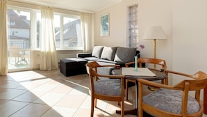 A living room with a sofa, two wooden chairs, a small table, and a lamp. - Apartment in Rewal Near the Beach (Rewal)