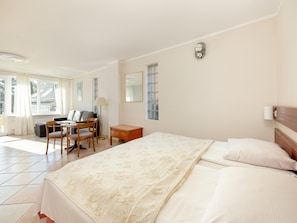 A hotel room with a large bed, a desk with a chair, a lamp, and a window with curtains. - Comfortable Holiday Studio, Breakfast Included (Rewal)