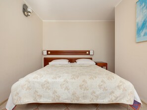 A neatly made bed with a floral-patterned bedspread, a wooden headboard, and a bedside table with a lamp. - Comfortable Holiday Studio, Breakfast Included (Rewal)
