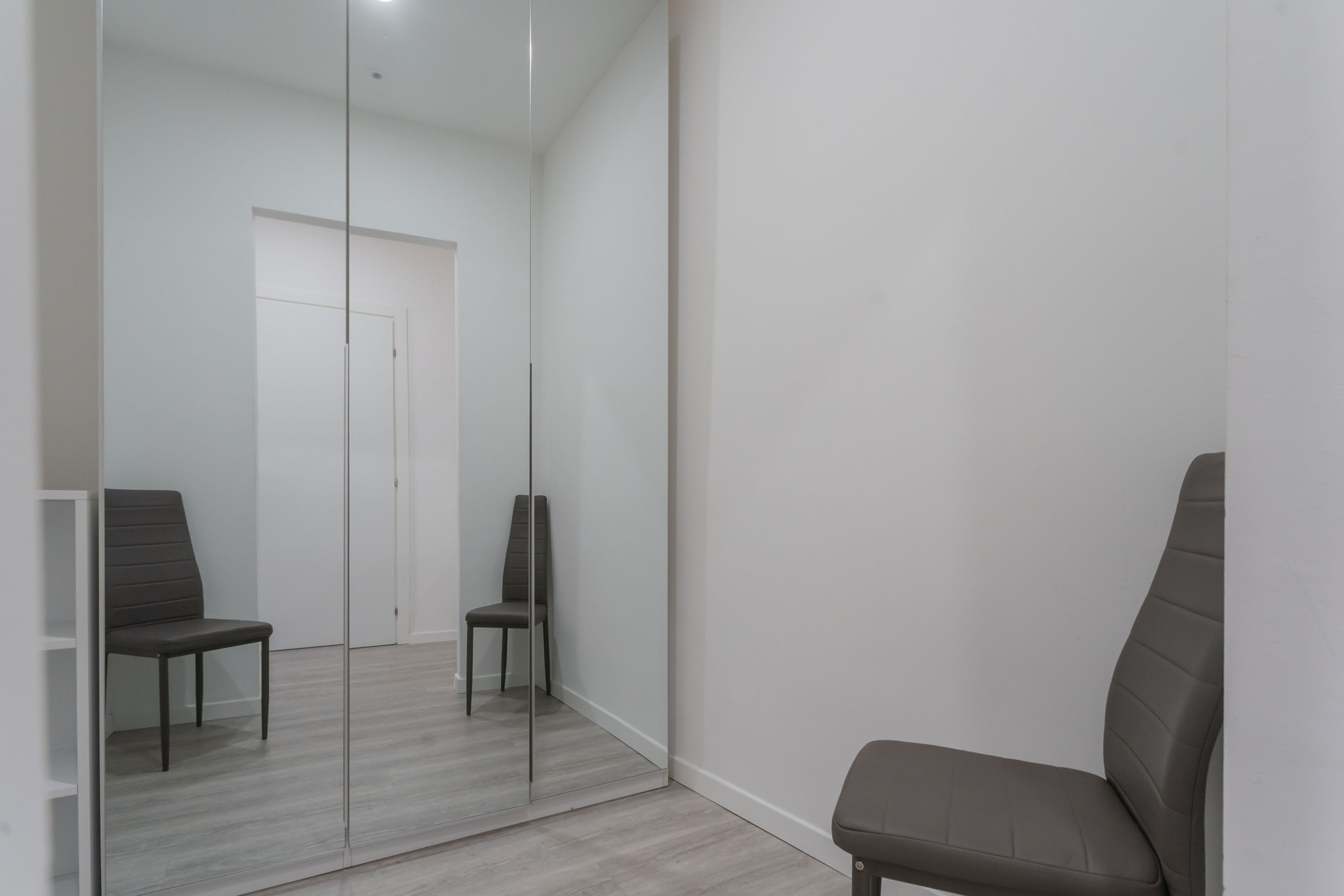 A room with a mirrored closet door, two chairs, and a white door in the background.