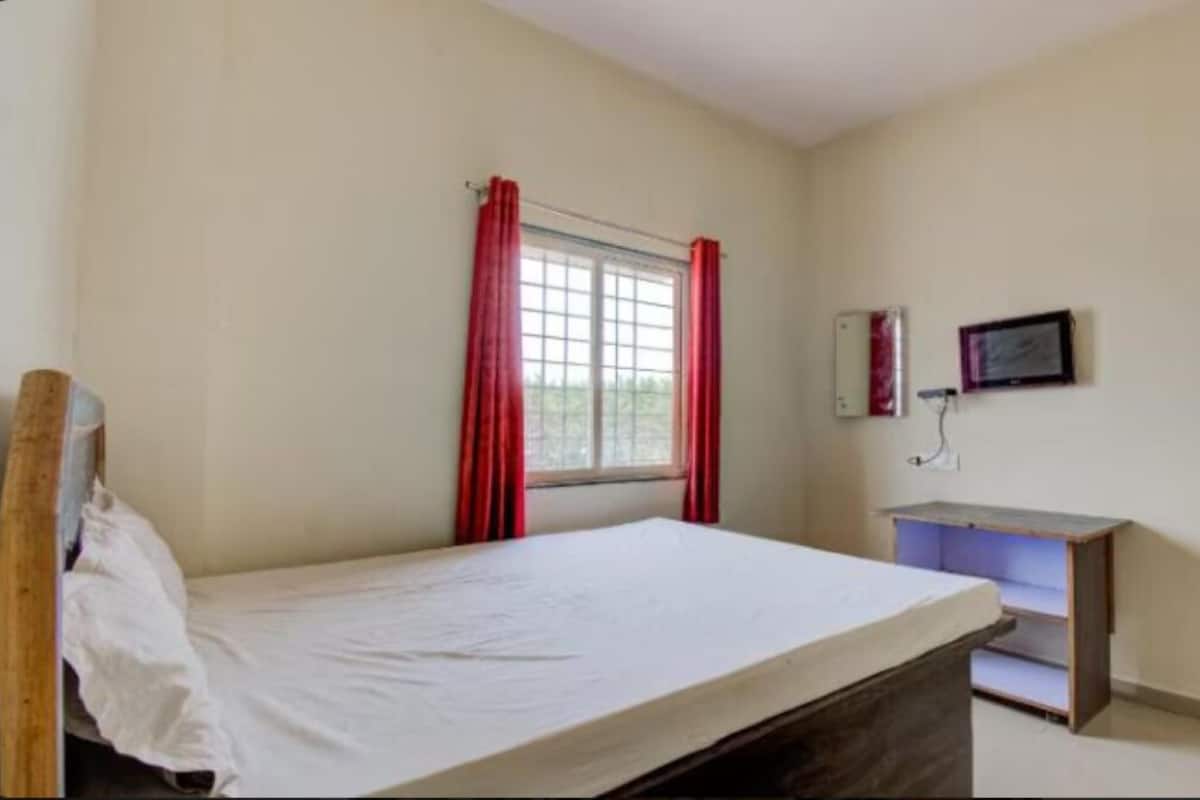Un letto singolo in una stanza con finestra, una piccola scrivania e uno specchio fissato alla parete.