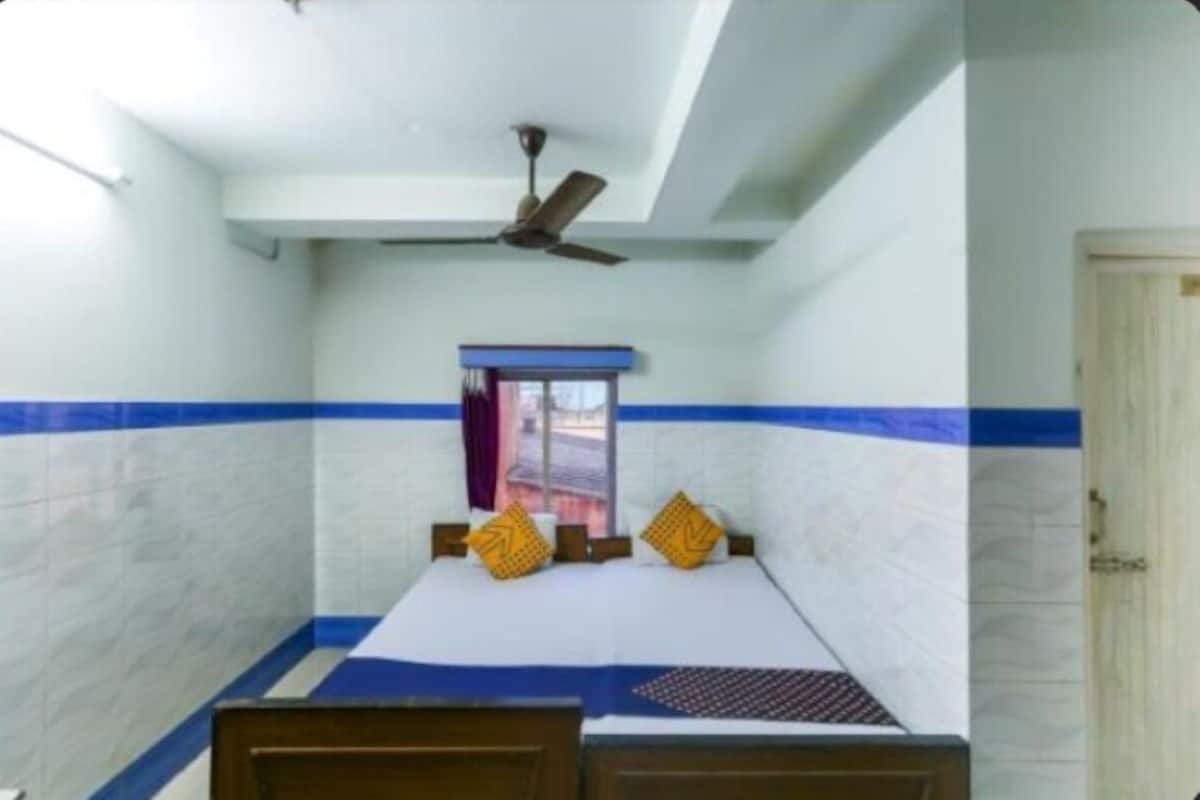Una camera piccola con un letto singolo, un ventilatore a soffitto, una finestra con tenda e una porta.