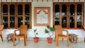 A room with wooden-framed windows, a framed artwork on the wall, and two potted plants. - Ganga Bitan Family Inn (Uluberiya)