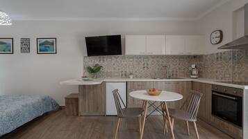 A compact kitchen with a dining area, a flat-screen TV, and a clock on the wall.
