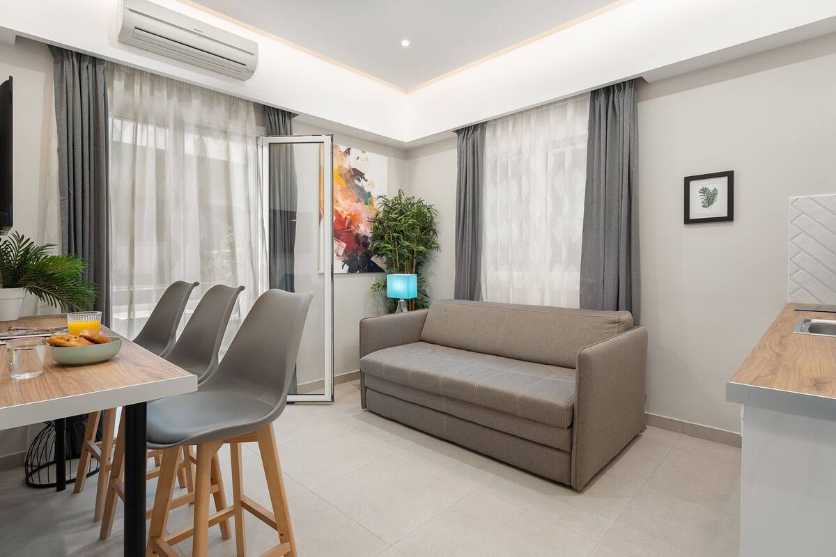 A modern living room with a sofa, dining table, chairs, and a kitchen area.