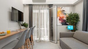 A modern living room with a grey sofa, a dining table with chairs, a flat-screen TV, and a large window with sheer curtains.