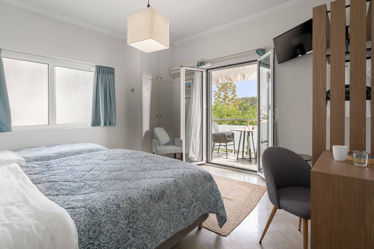 A bedroom with a bed, a desk, and a chair. There is a sliding glass door leading to an outdoor area.