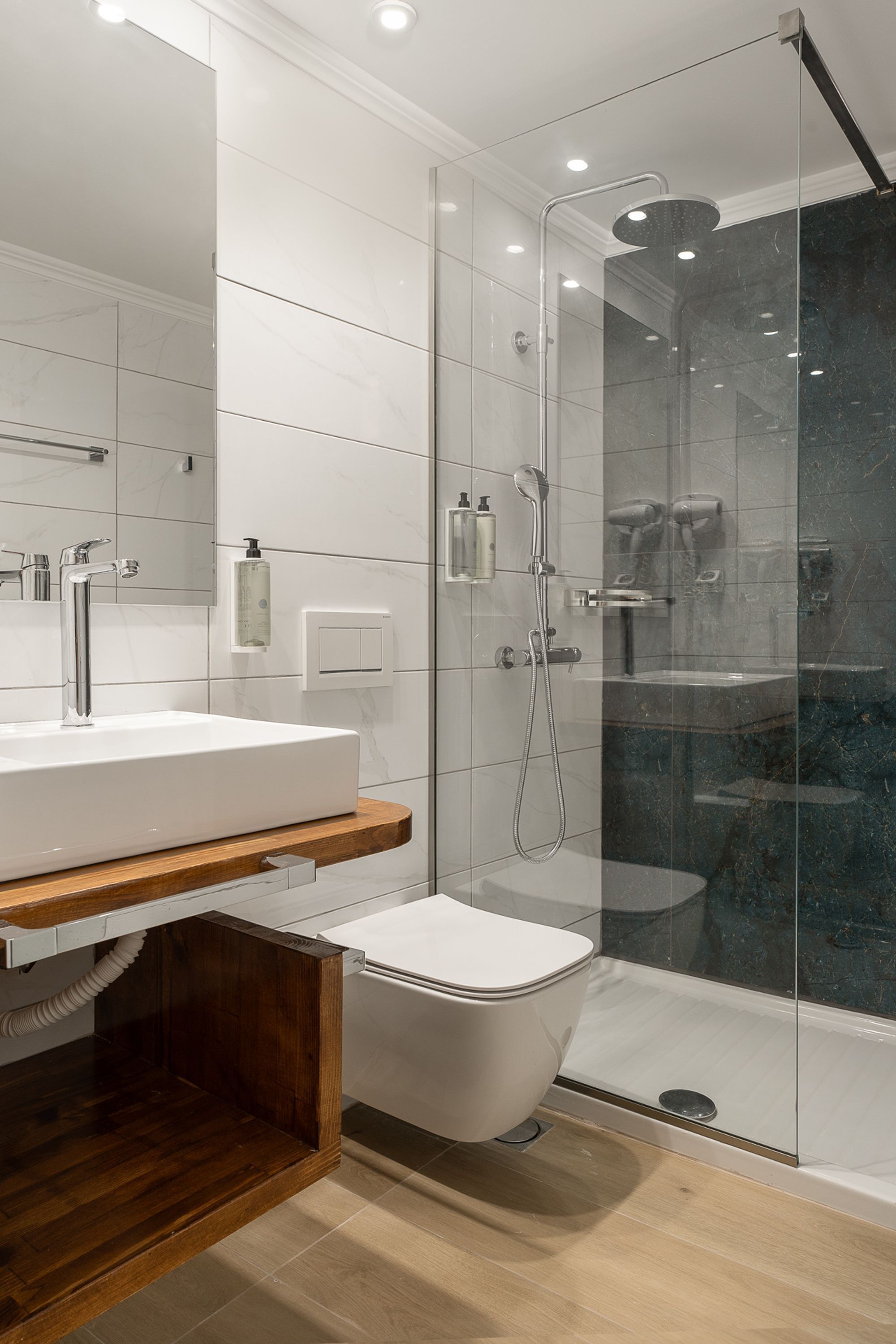 A modern bathroom with a glass-enclosed shower, a white sink, and a wooden vanity.