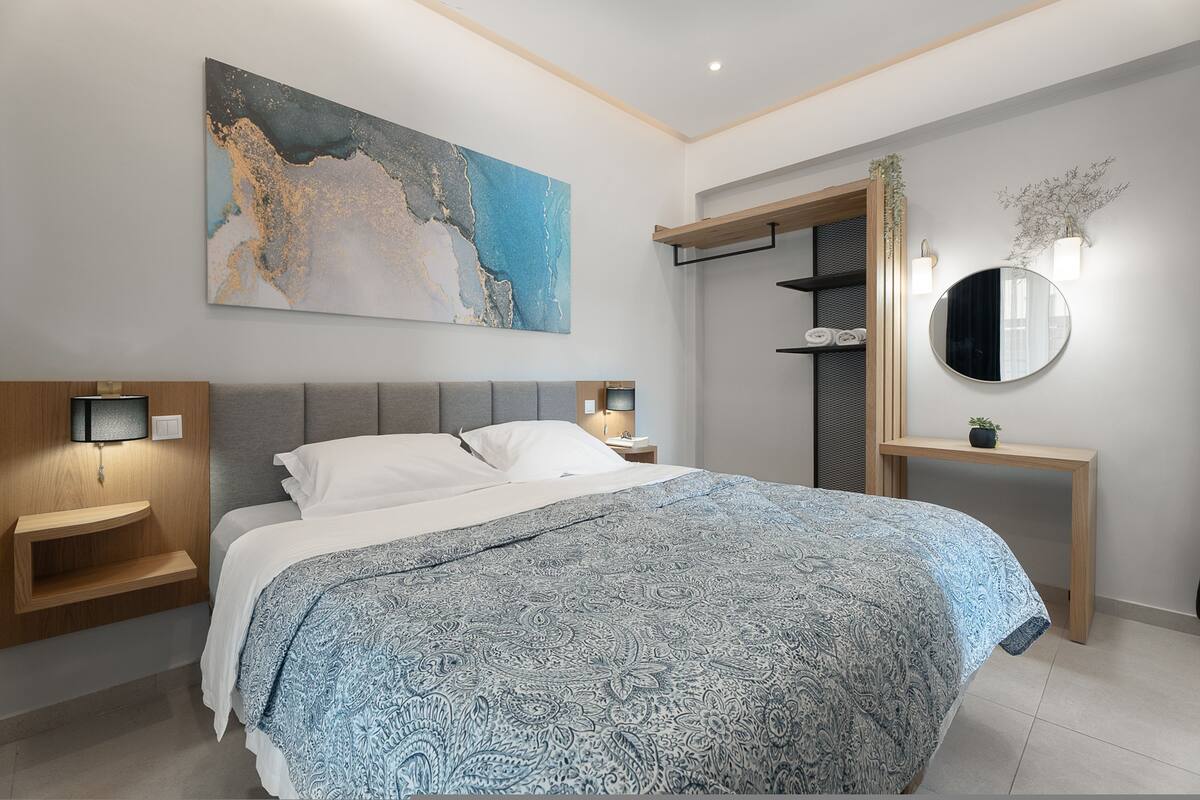 A modern bedroom with a large bed, bedside tables, a wall-mounted TV, and a large abstract painting.