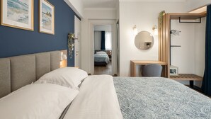 A bedroom with a large bed, a desk, a chair, a mirror, and two framed pictures on the wall.
