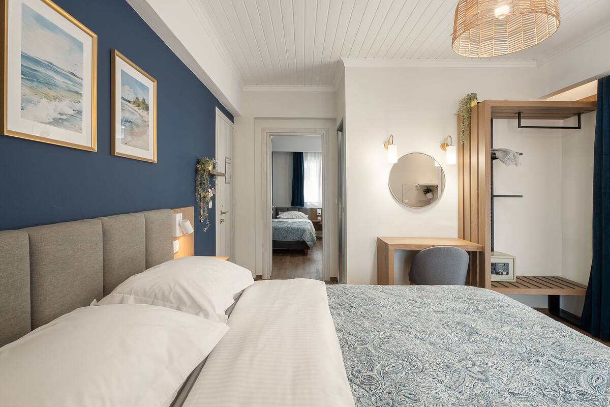 A bedroom with a large bed, a desk, a chair, a mirror, and two framed pictures on the wall.
