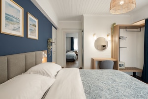 A bedroom with a large bed, a desk, a chair, a mirror, and two framed pictures on the wall.