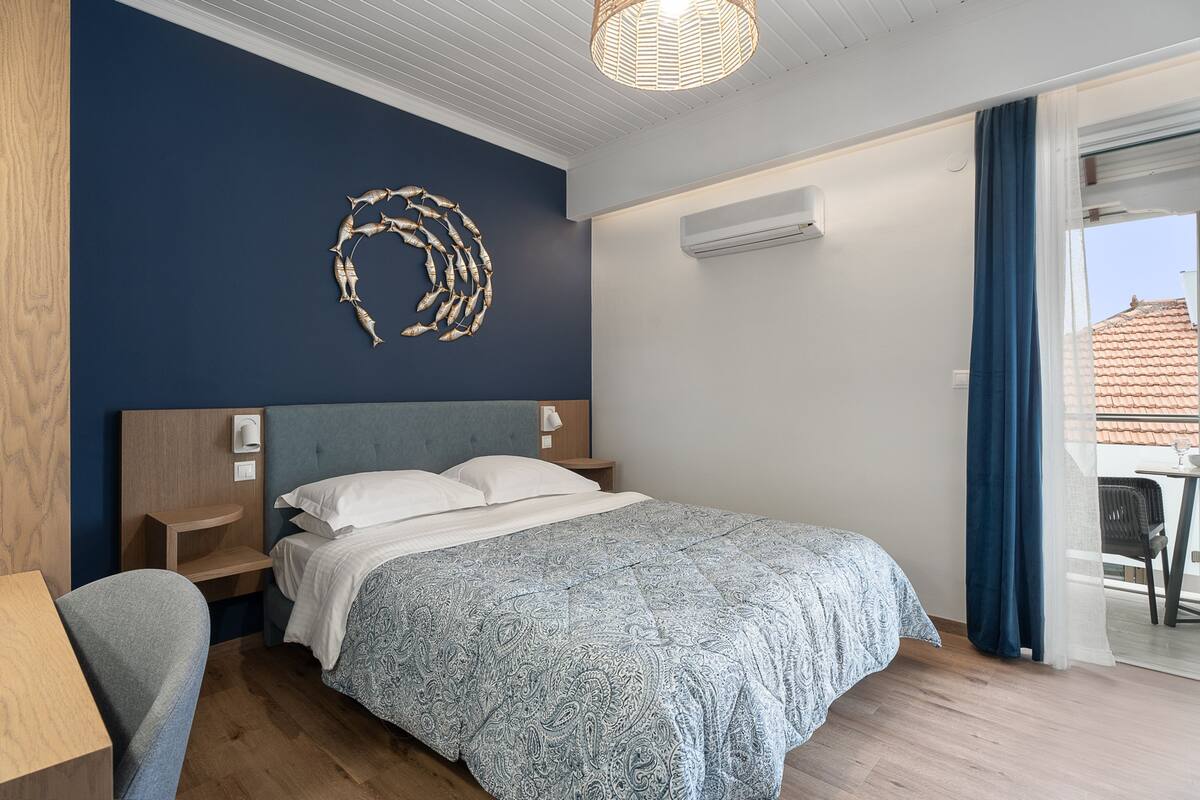 A bedroom with a bed, bedside tables, a wall-mounted air conditioner, and a view of the outside.