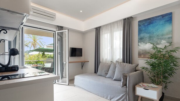 A modern hotel room with a sofa, a small side table, a TV, and a large window with curtains.