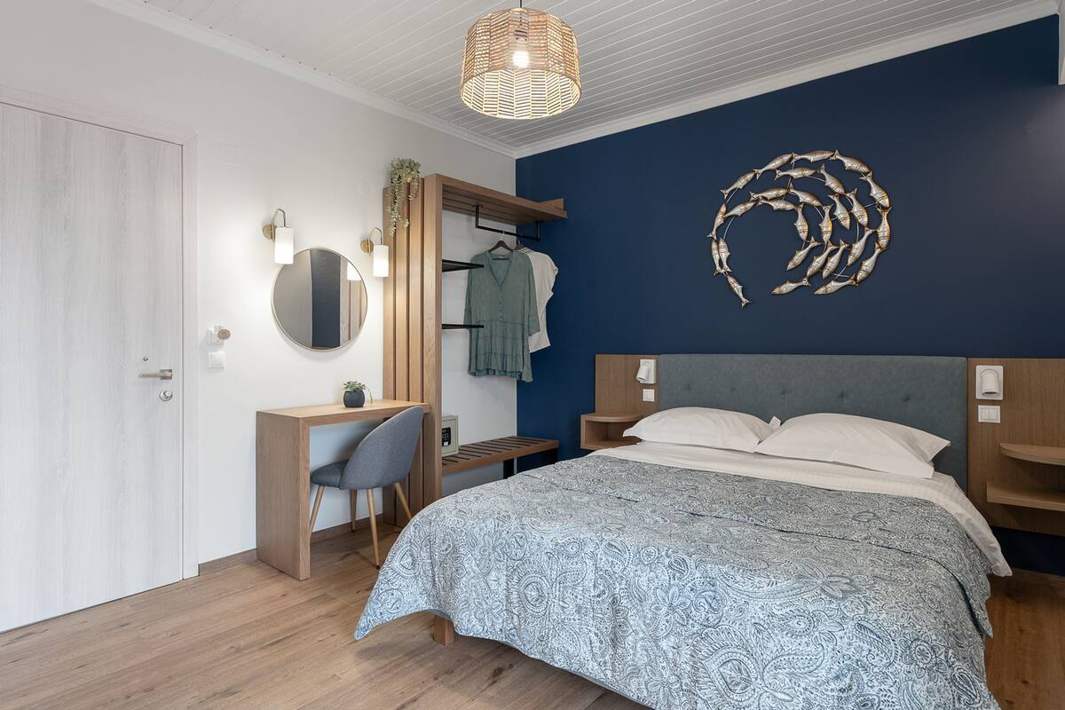 A bedroom with a bed, a desk, a chair, a wardrobe, a mirror, and a wall art piece.