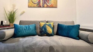 A grey sofa with three cushions, one with a tropical leaf pattern, in a room with a painting of an elephant on the wall. - 3 bed cosy home parking & wi-fi (Leicester)
