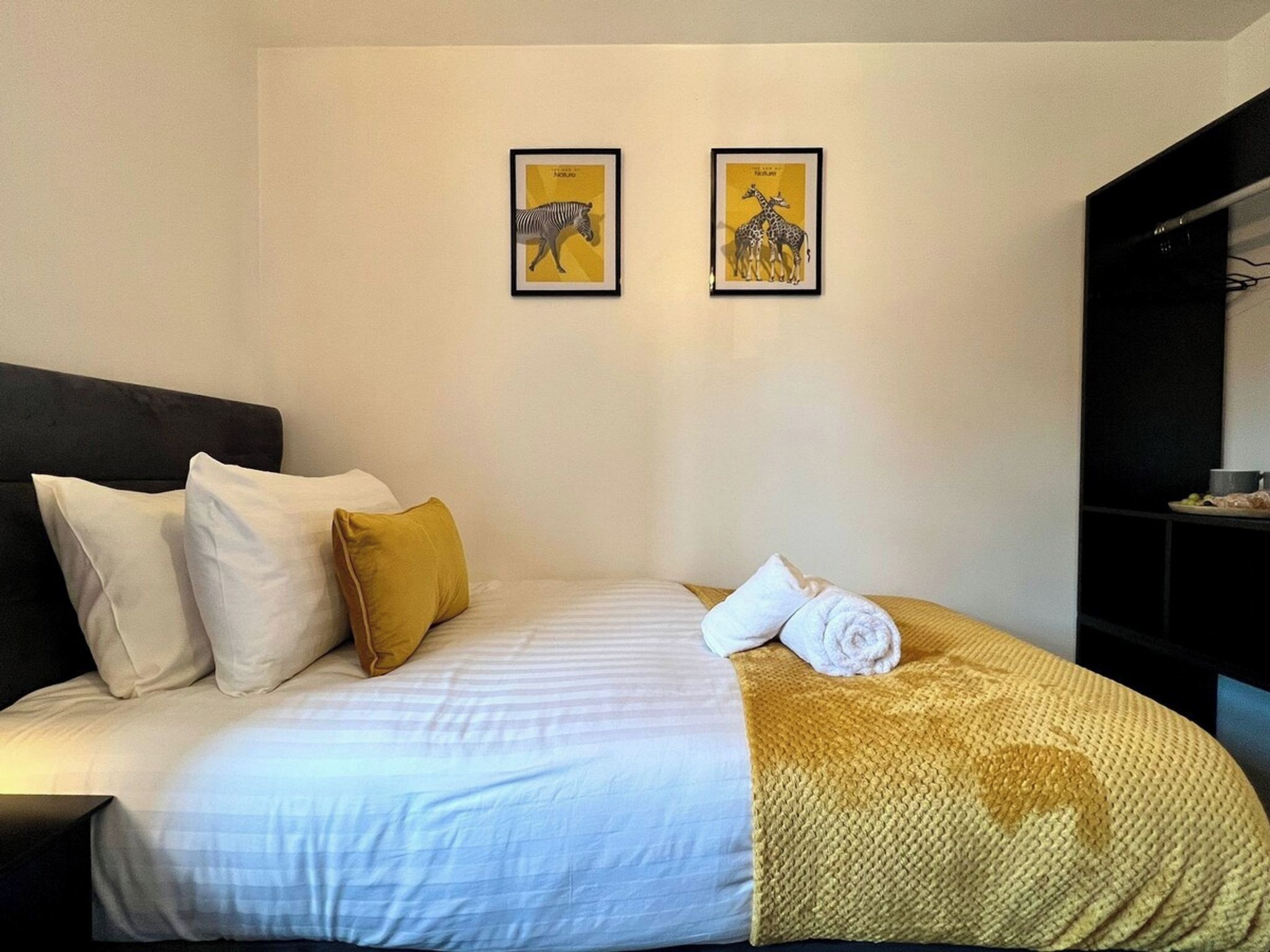 Ein Hotelzimmer mit einem Bett, Kissen, einer Decke und zwei gerahmten Bildern an der Wand.