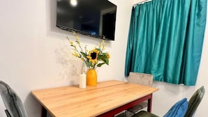A dining area with a wooden table, two chairs, a vase with flowers, a candle, and a TV mounted on the wall. - 3 bed cosy home parking & wi-fi (Leicester)