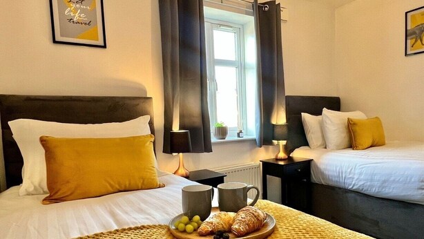 A hotel room with two beds, a breakfast tray with croissants and grapes, and a framed quote on the wall. - 3 bed cosy home parking & wi-fi (Leicester)