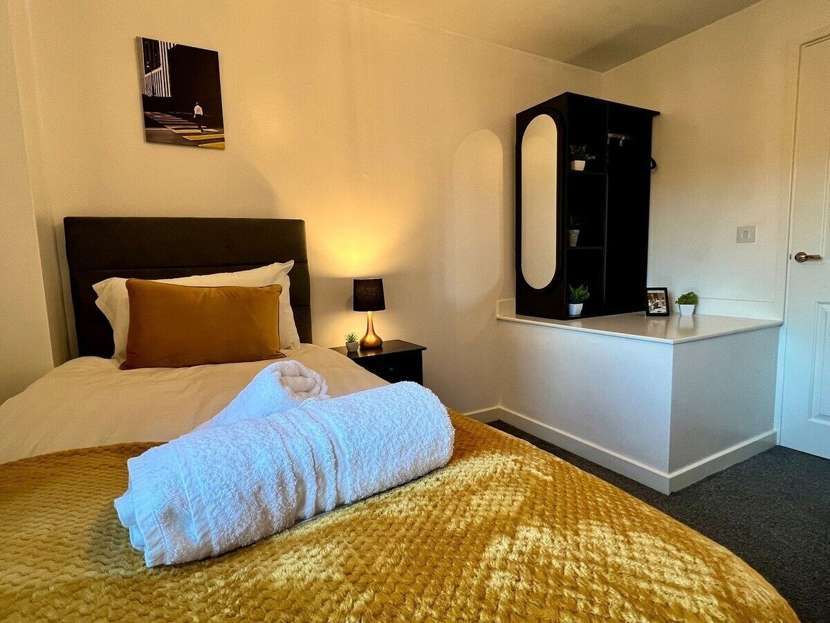 Une chambre d’hôtel comprenant un lit, une table de chevet avec une lampe, un miroir et une petite étagère ornée d’objets décoratifs.