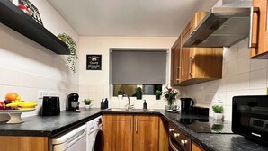 A compact kitchen with wooden cabinets, a built-in dishwasher, a microwave, and a coffee maker. - 3 bed cosy home parking & wi-fi (Leicester)
