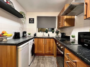 Una cocina compacta con armarios de madera, lavavajillas integrado, microondas y cafetera.