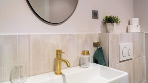 A bathroom with a white sink, gold faucet, and a round mirror. There is a potted plant, a glass jar, and a towel on the wall. - Pied-à-terre (Zadar)