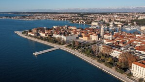 An aerial view of a coastal city with a prominent waterfront, a central square, and a mix of historical and modern buildings. - Pied-à-terre (Zadar)