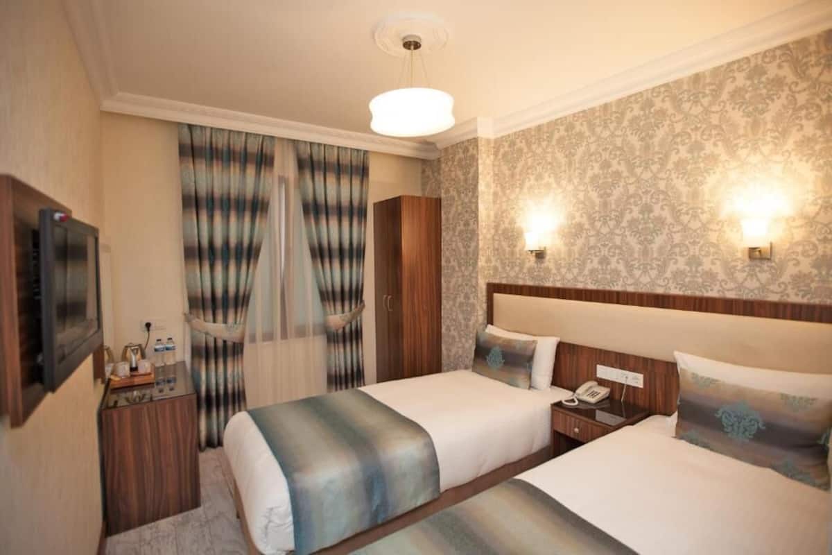 A hotel room with two beds, a nightstand, a TV, and a large window with curtains.