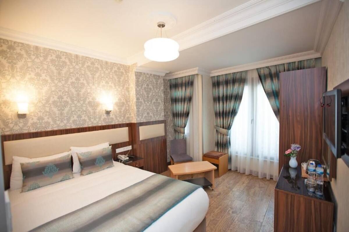 A hotel room with a large bed, a desk, a chair, a TV, and curtains.